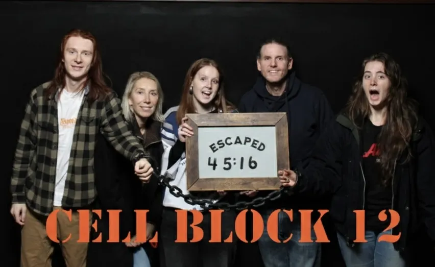 Ammon and his family in front of a CELL BLOCK 12 backdrop, holding a sign that reads 'ESCAPED 45:16'