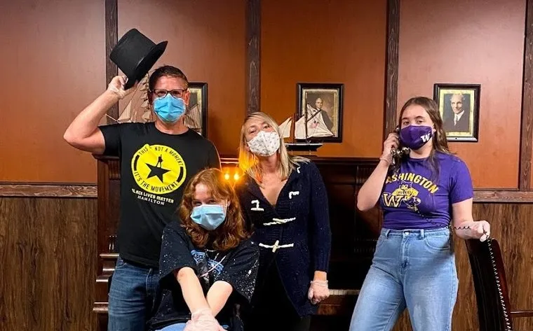 The family in face masks in a wood-panelled study hung with portraits, one tipping a top hat and one listening on an old telephone